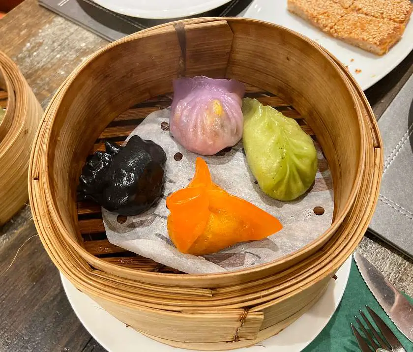 Assorted purple, orange, green and black dim sum in a bamboo container