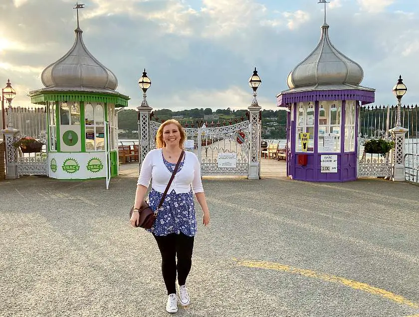 Mel walking in front of the entrance to Bangor Garth Pier at sunset 