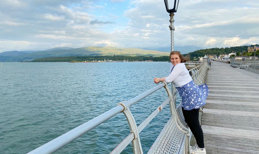 Mel posing on the Bangor Pier on a windy day with mountains in the background