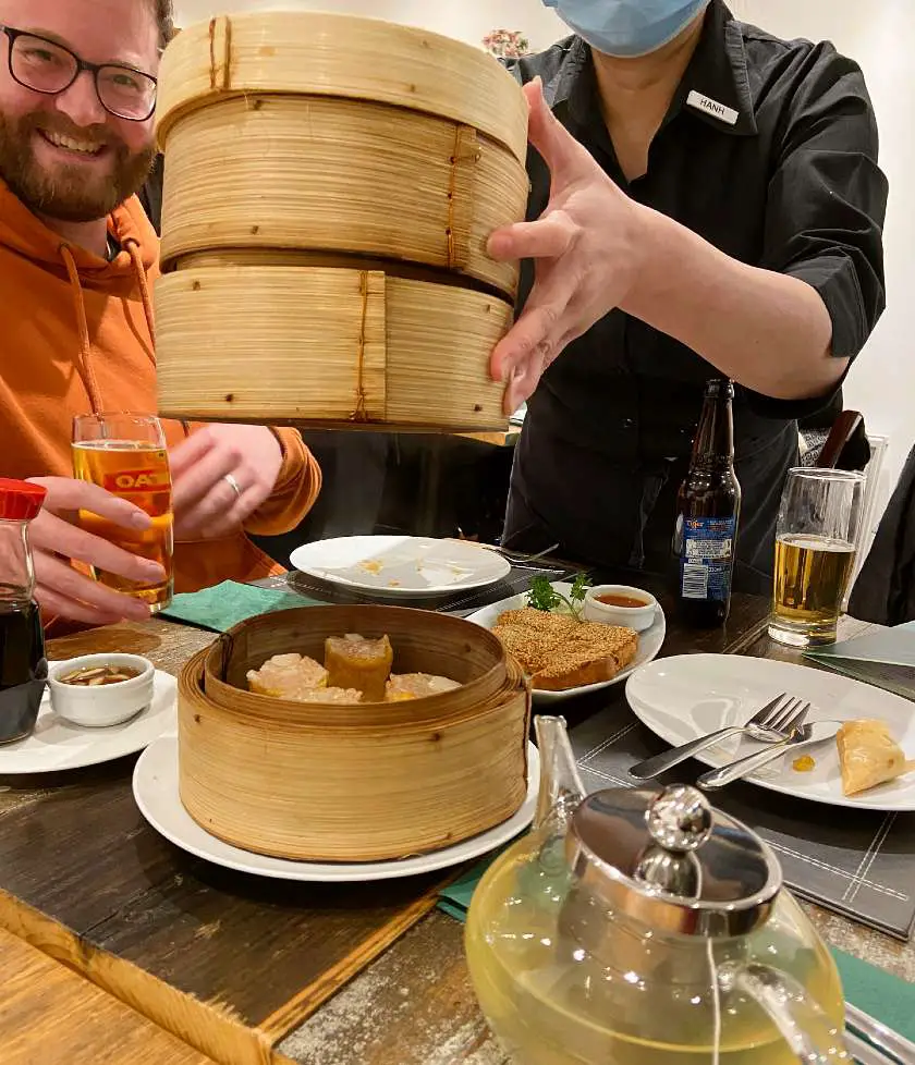 Waitress lifting bamboo containers with sui mai vegan pork dumpling in the bottom container