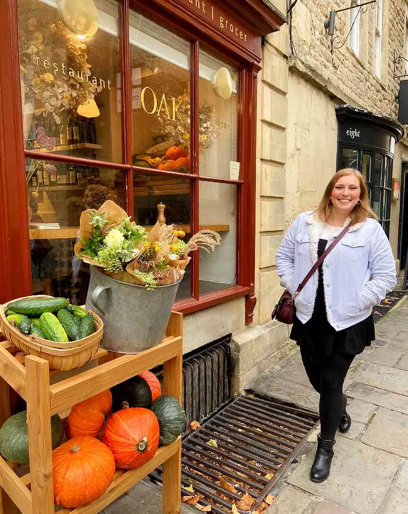 Mel walking in front of Oak restaurant in the North Passage of Bath with flowers and pumpkins outside