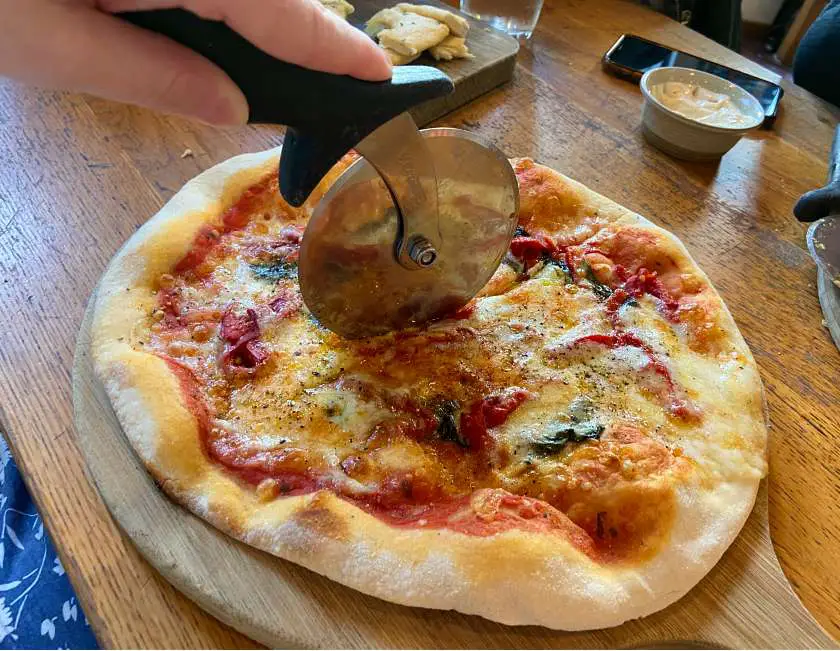 Pizza cutter cutting into margarita pizza on a wooden board