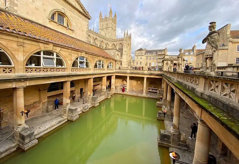 View of the main Roman Bath green pool in Bath with the Cathedral in the background