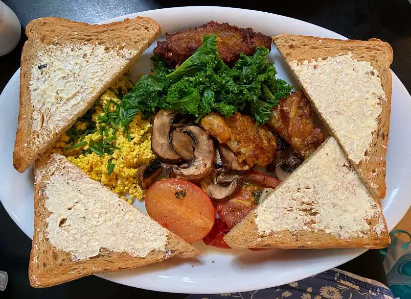 Vegan full english breakfast with buttered toast, hash browns, scrambled tofu, tomatoes, mushrooms and kale