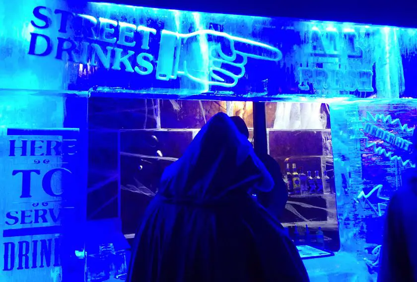 Main bar in Ice Bar London lit up in blue with a person in a hooded snow jacket waiting to be served