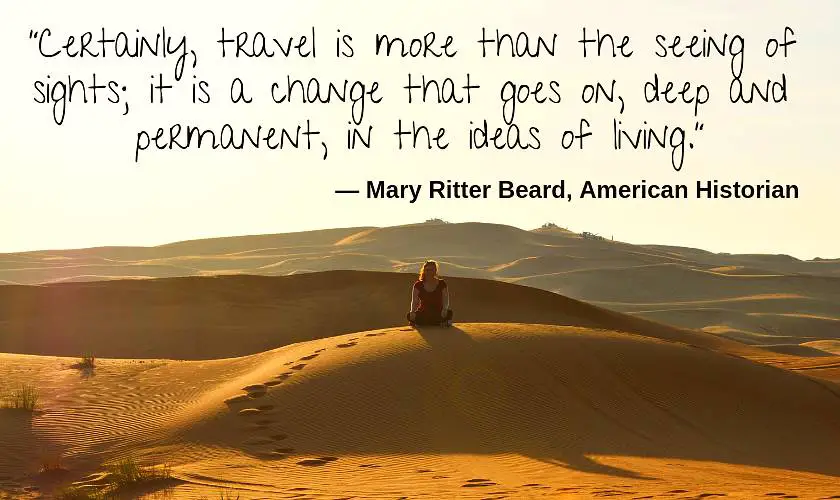 Mel on top of a sand dune with her legs crossed in the Dubai desert with the quote: “Certainly, travel is more than the seeing of sights; it is a change that goes on, deep and permanent, in the ideas of living.” by Mary Ritter Beard, American Historian 