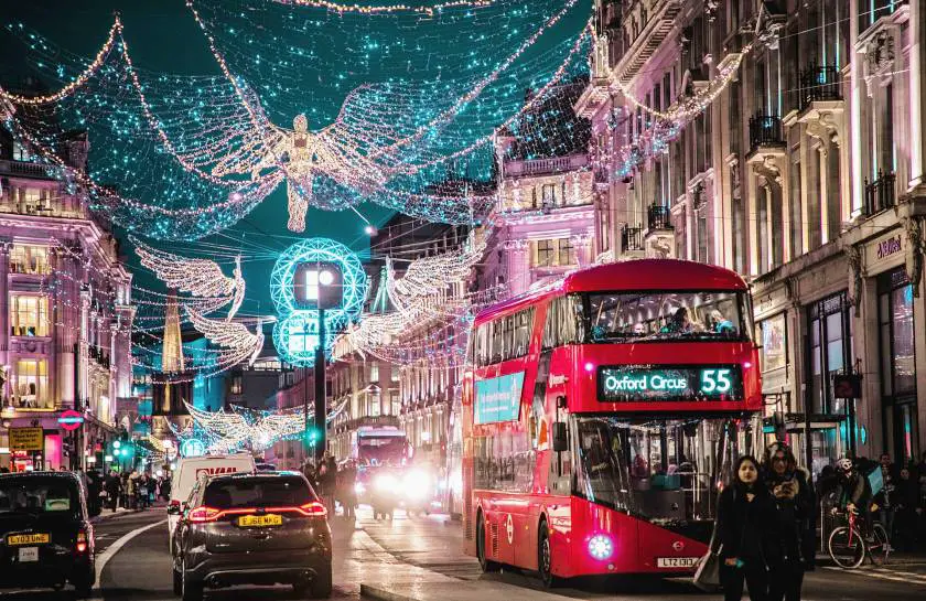 Oxford Street in London with Christmas lights strewn above the street and cars and red buses going by at night