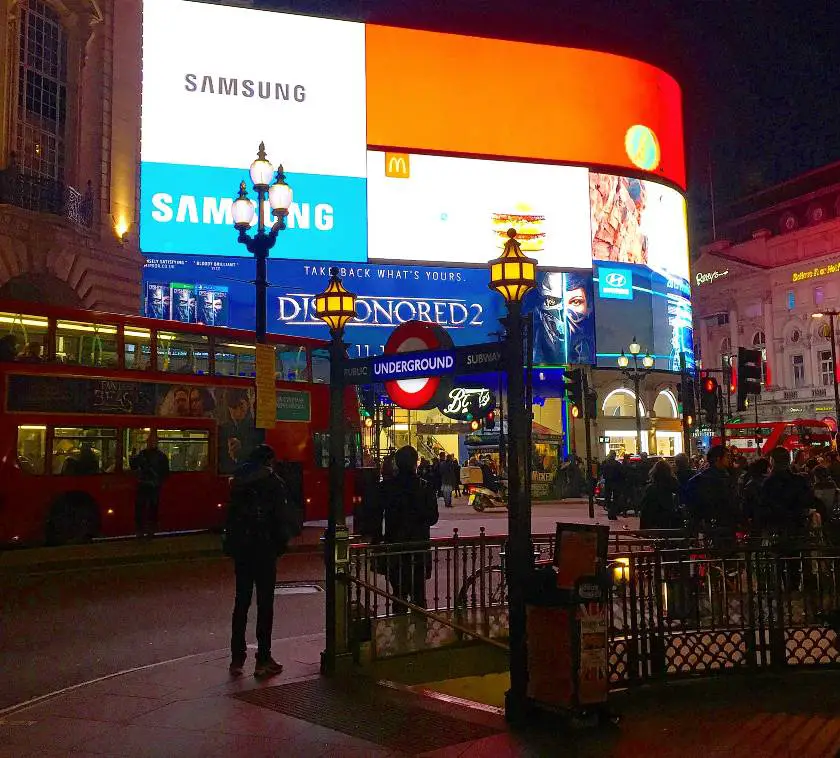 Front of the London underground at Piccadilly Circus with the digital billboard in the background lit up at night time