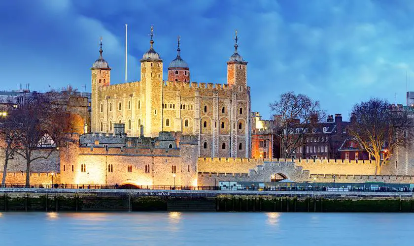 View of the white Tower of London lit up at night from the Thames river