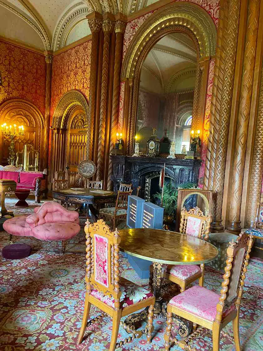 Inside of Penrhyn Castle in the luxurious gold and red sitting room with antique furniture and a large black fireplace