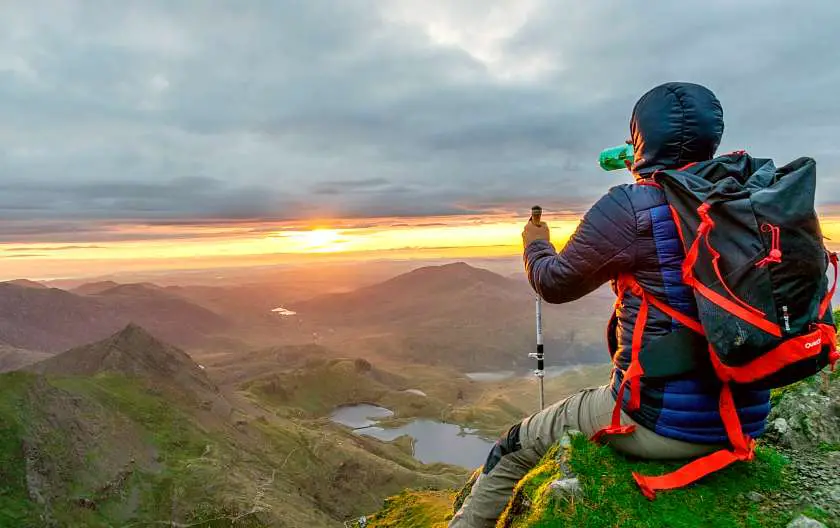 Hiker in a blue coat, sat down drinking water at the top of Snowdon at sunrise