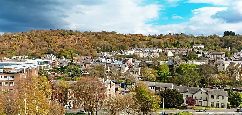 View of Bangor, Wales from Bangor University with rows of coloured small houses with green hills in the background a blue sky 