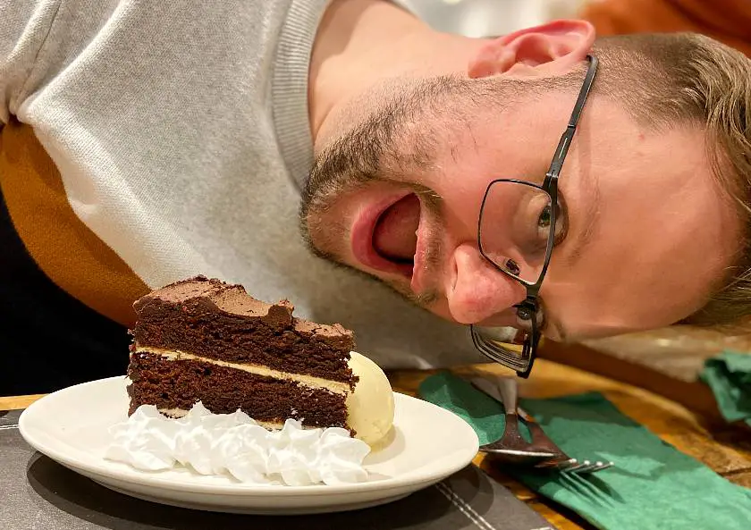 Mel's friend Ant with an excited face next to his vegan chocolate cake with coconut cream and ice cream