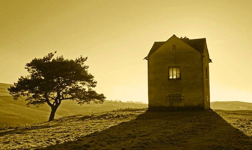 Old cottage on a hill in Lyme Park House and Gardens next to a tree at sunset