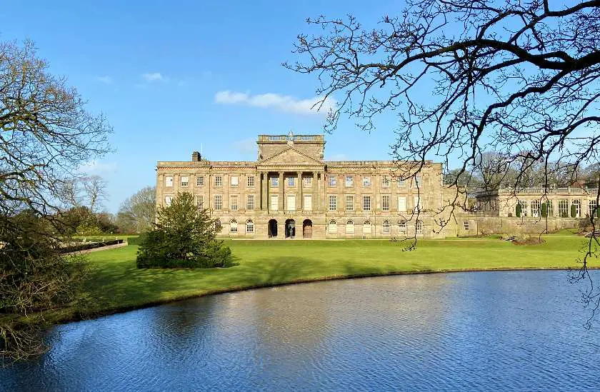 Lyme Park House, an elizabethan era building with trees and lake in the foreground against a blue sky