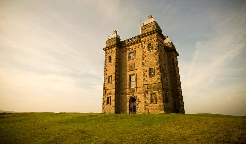 A tall foreboding Elizabethan building on a green hill at Lyme Park House and Gardens