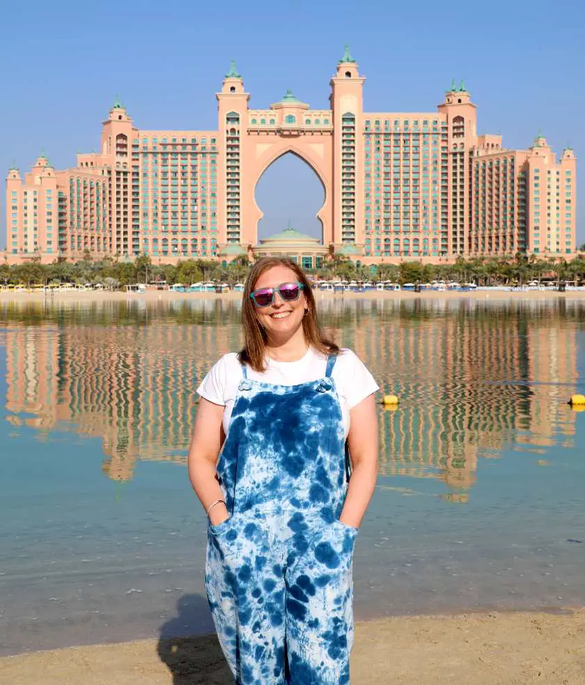 Mel in front of the Atlantis Hotel from a distance in Dubai wearing blue overalls and sunglasses