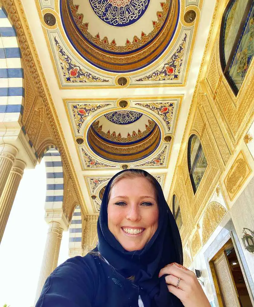 Selfie of Mel in an abaya with the ceiling of a yellow and blue detailed mosque 