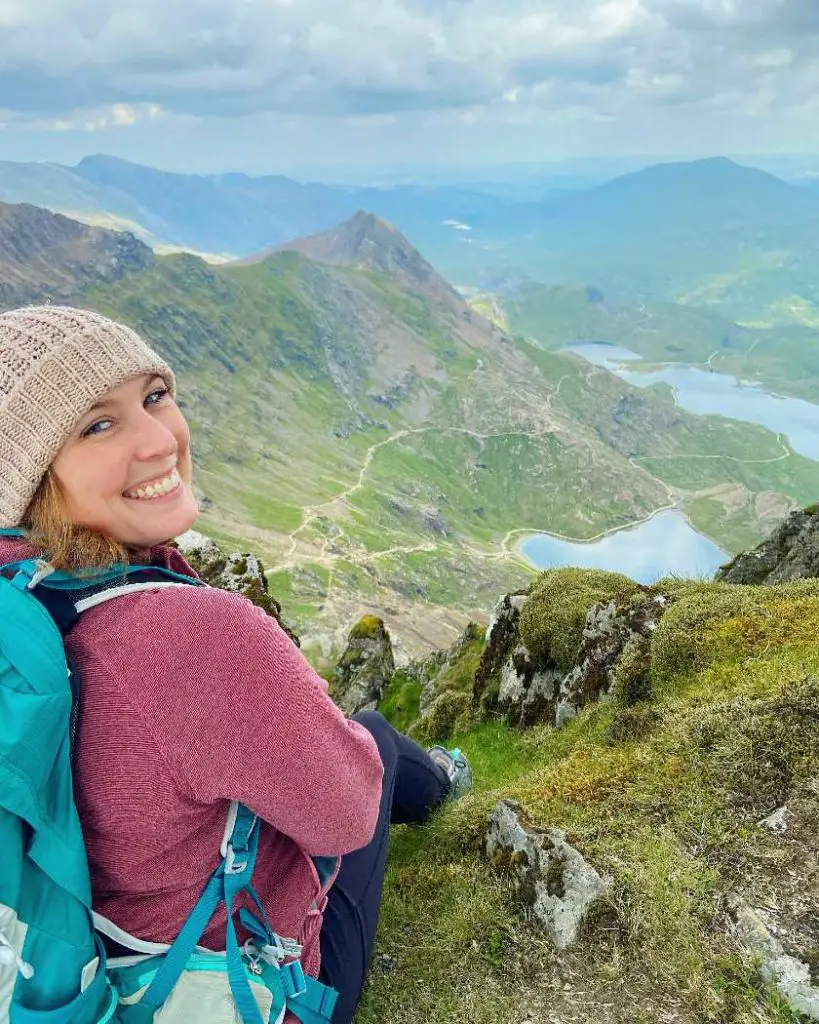 Mel sat at the summit of Snowdon in Wales with lakes and peaks in the background