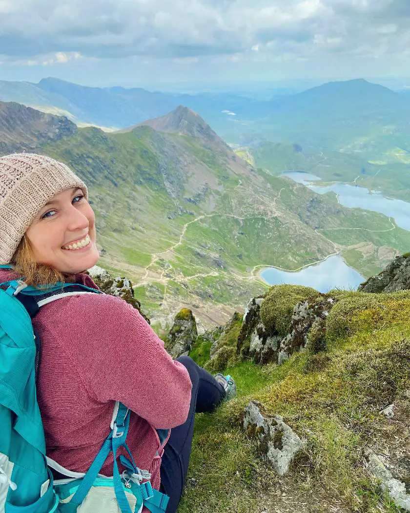 Close up image of Mel smiling from the top of Snowdon with lakes and peaks in the background