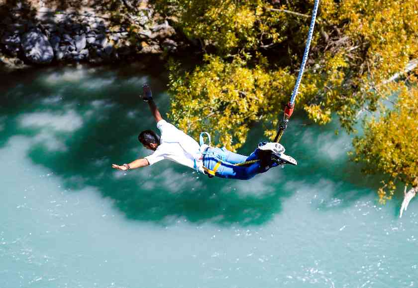 Man bungee jumping up close with his arms out over a river and trees