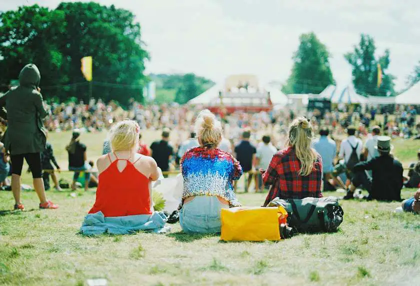 Three girls sat with their backs to camera at a busy festival in a field