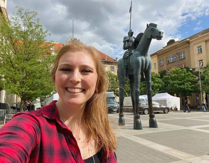Mel in a red shirt taking a selfie in front of the famous brno horse and guard statue