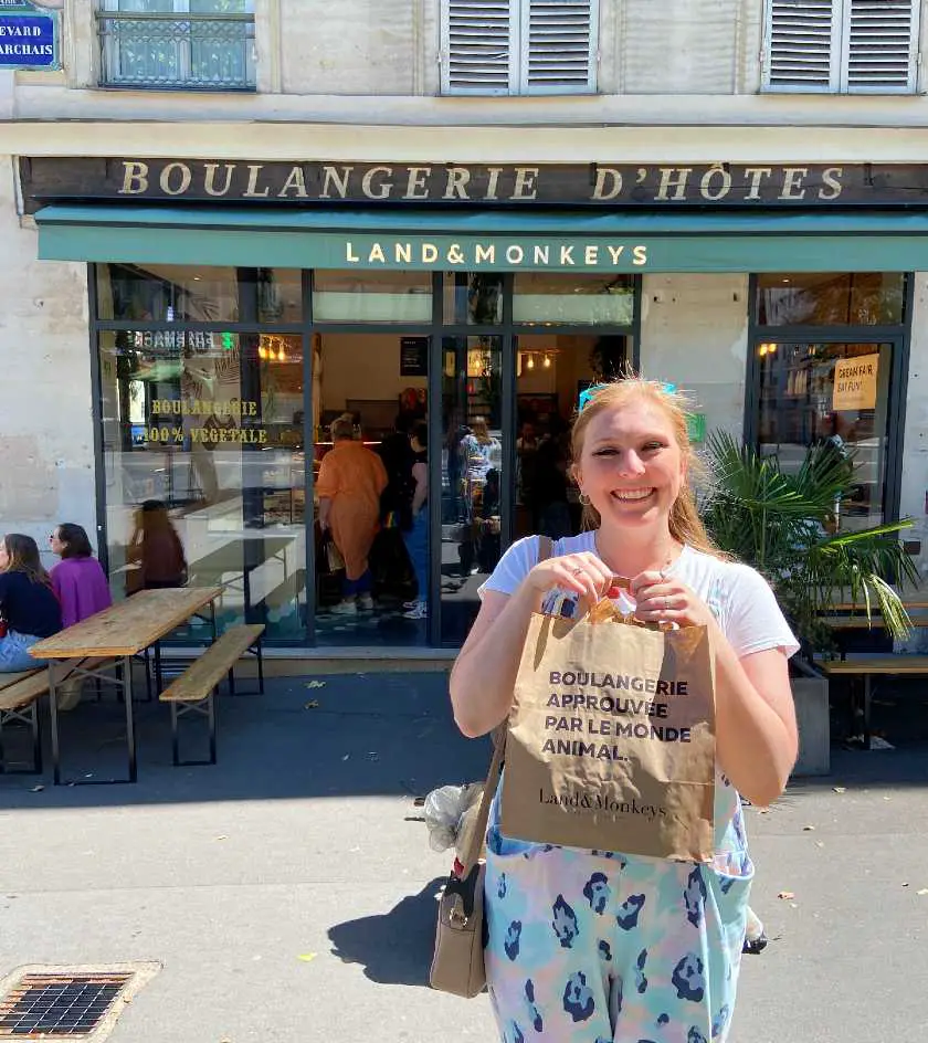 Mel holding a paper bag of pastries up outside Land and Monkeys bakery in paris 
