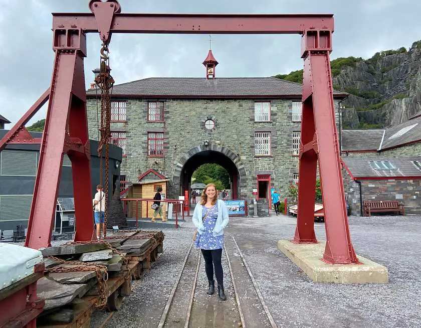 Mel in front of the National Slate Museum in Wales, a victorian building with red industrial steel around it