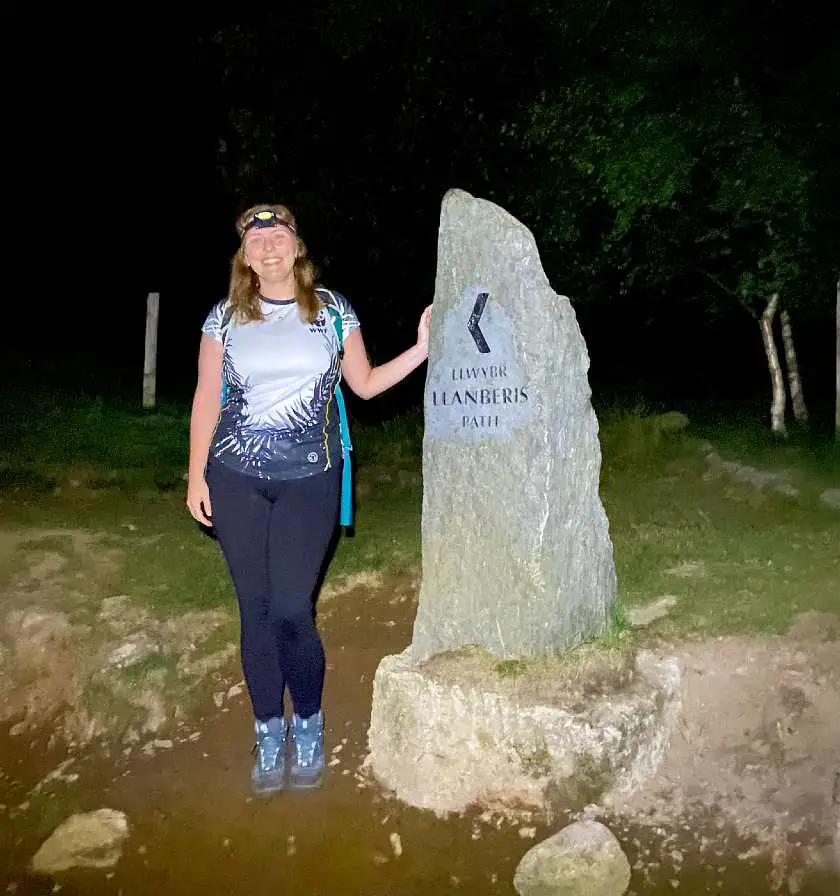 Mel stood by the Llanberis Path's stone marker whilst climbing Snowdon in the dark with a head torch on