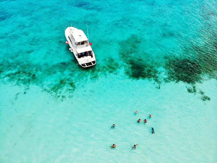 Drone shot of a white boat in the ocean and people swimming nearby