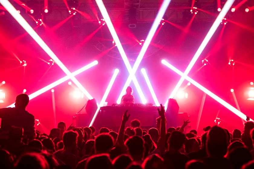 DJ with a crowd in front of them in a nightclub with red strobe lights behind