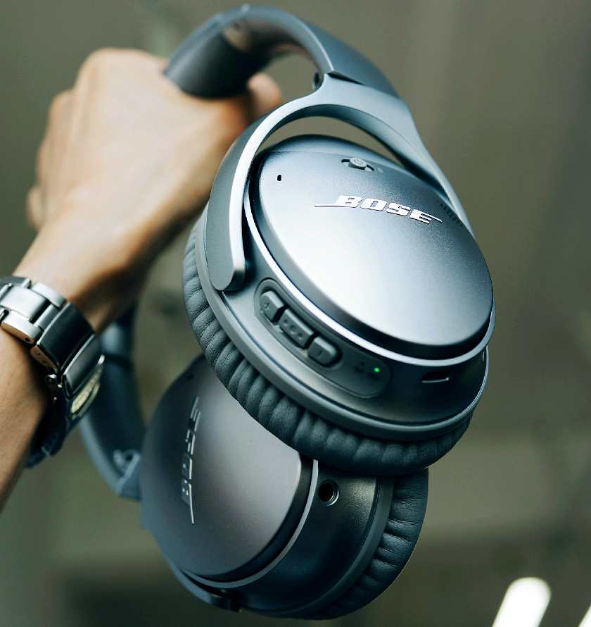 A hand holding a pair of Bose noise cancelling headphones