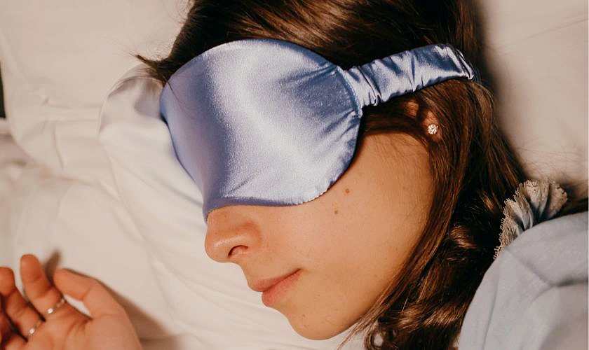 Woman lying down wearing a blue sleeping mask over her eyes