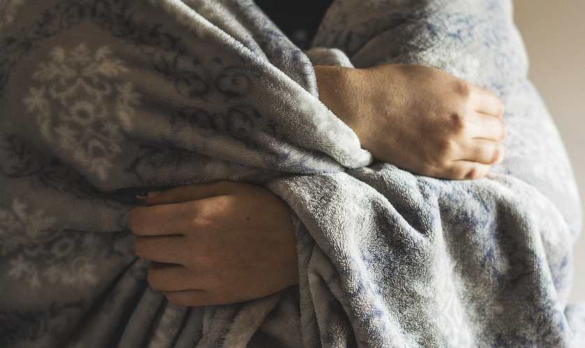A woman holding a grey blanket around her holding it with her hands