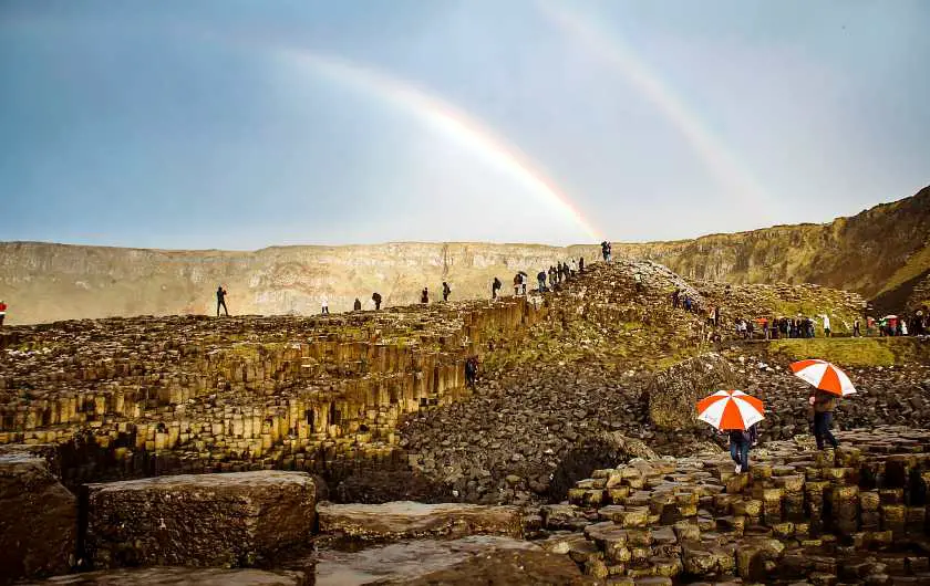 Two rainbows over the Giant's Causeway with people holding up umbrellas underneath