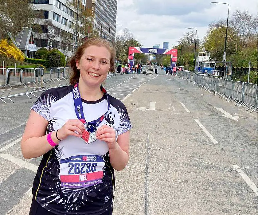 Mel holding her Manchester marathon medal in front of the finish line