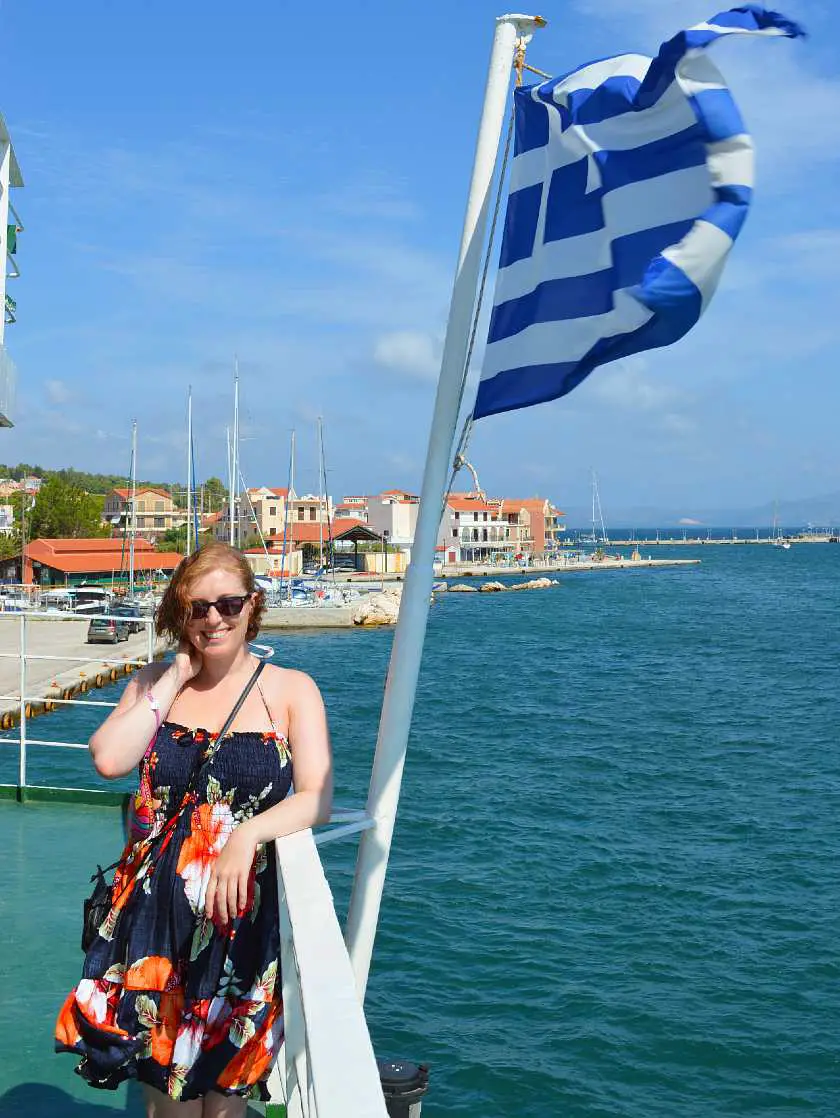 Mel smiling on a boat headed out of Kefalonia next to a Greek flag blowing in the wind