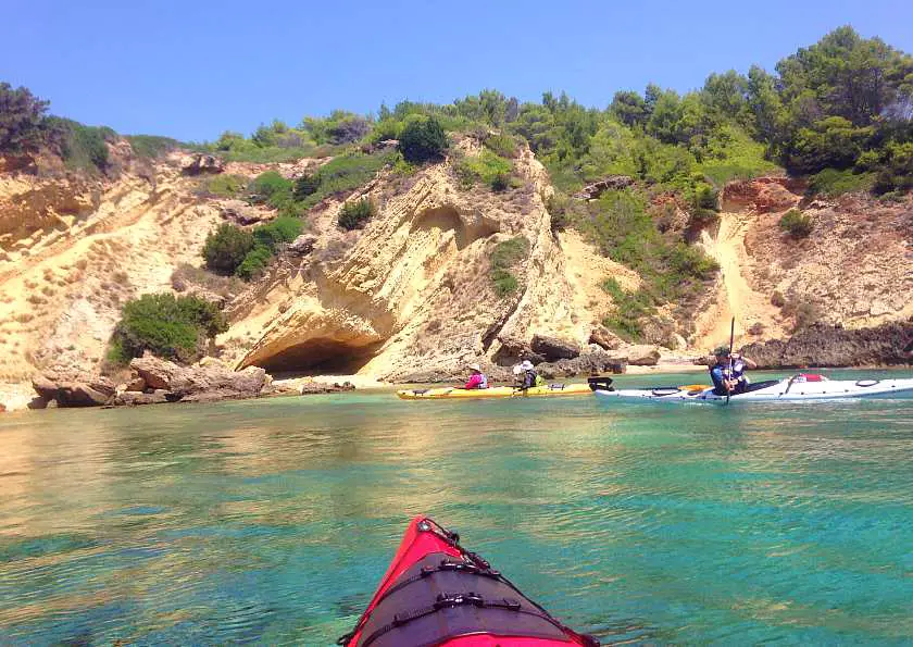Photo taken from a red kayak of white a rock face from the sea with other kayakers in the background 