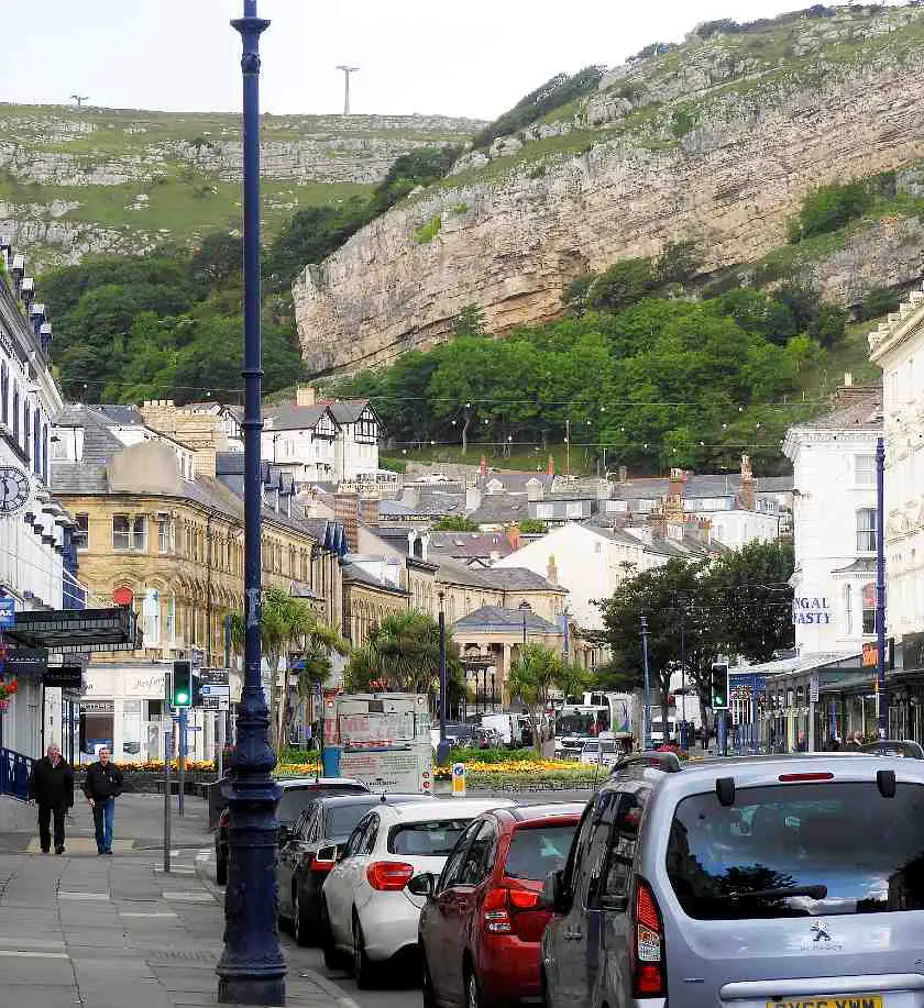 Mostyn Street in Llandudno Wales with shops either side and a row of parked cars in the background