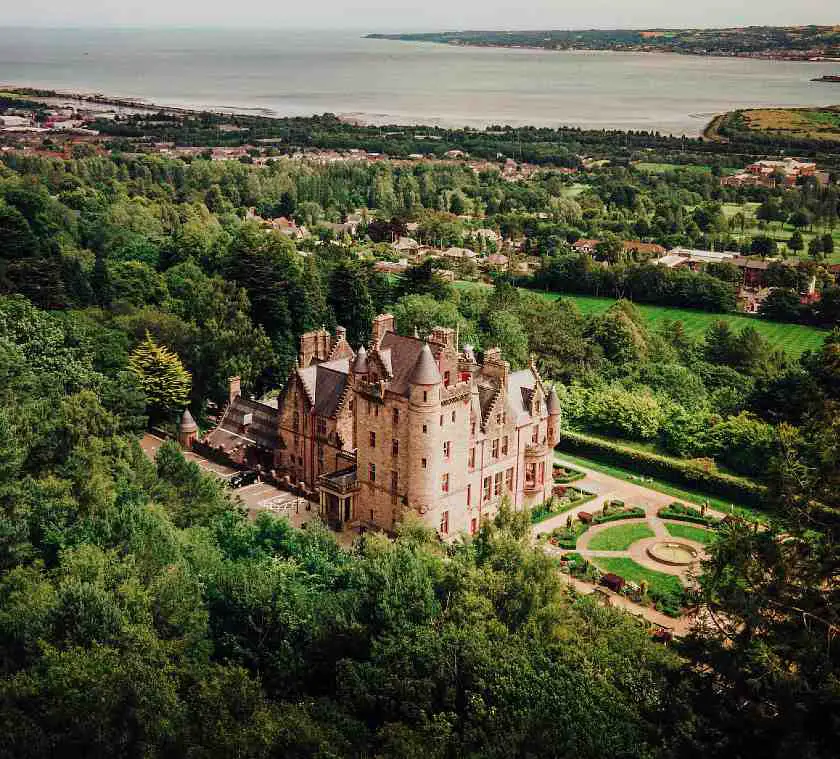 Belfast Castle taken from above amongst lots of greenery and the coast in the background