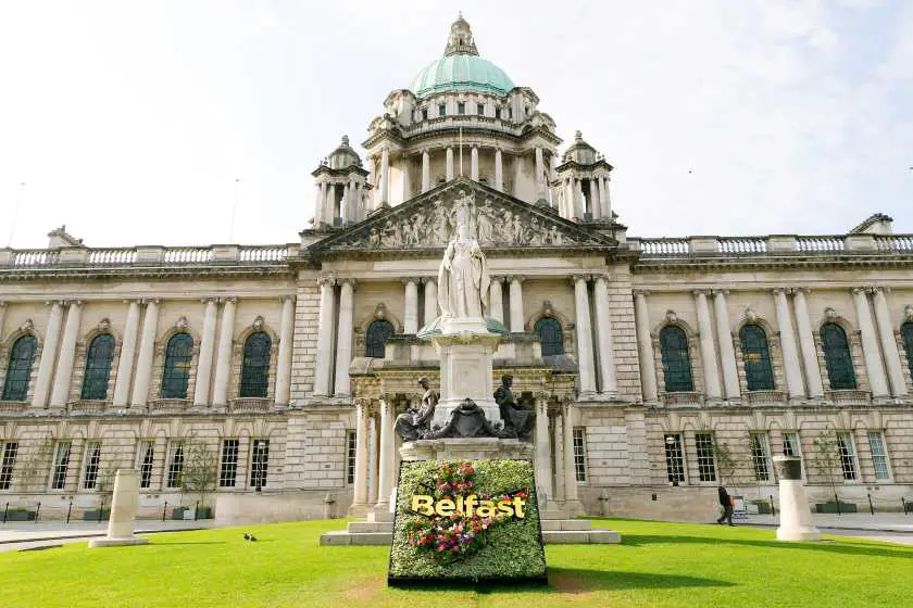 Outside the Belfast City Hall, a white victorian hall building with a statue of Queen Victoria outside on a green lawn