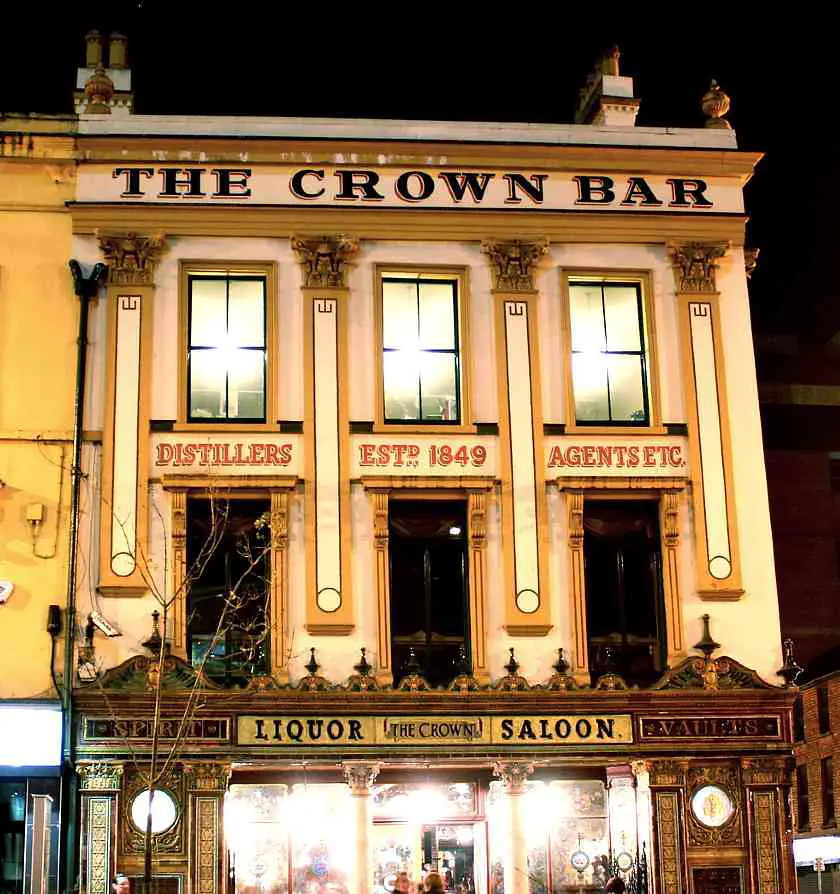 Outside the Crown Liquor Saloon or Crown Bar at night, a victorian style white building with a green tiled and gold grand front entrance