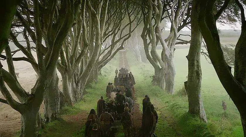 Screenshot of the Dark Hedges in the Game of Thrones with actors pulling carts down the road on the way to King's landing in the show 