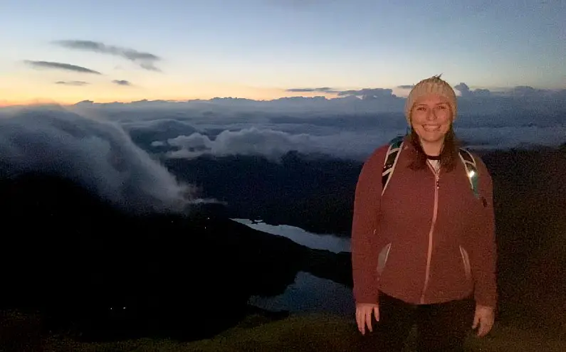 Mel smiling in front billowing clouds as the sun peaks over the distance over Snowdon