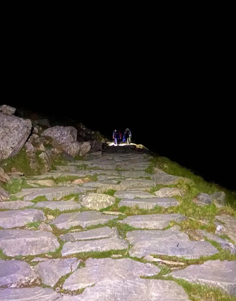 Llanberis Path in the dark with a torch light on the ground and hikers in the background
