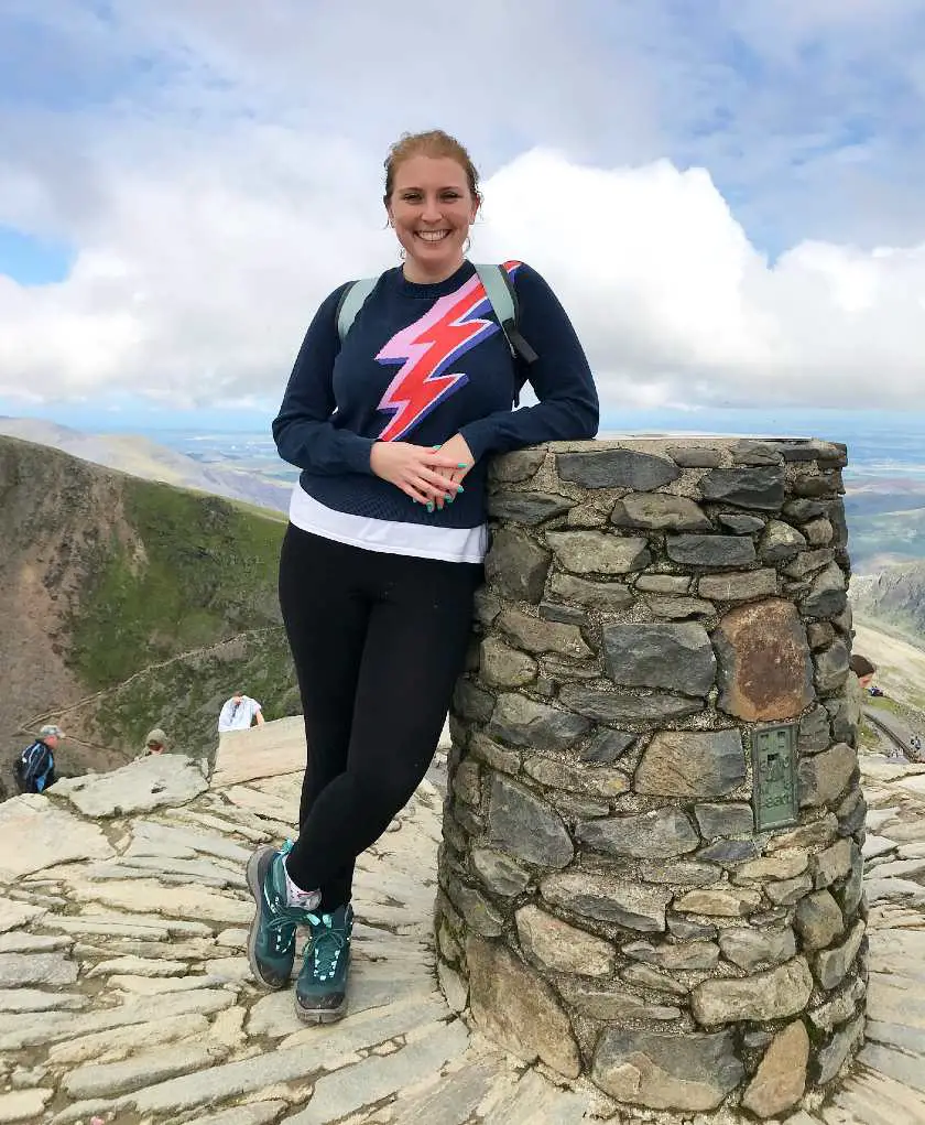 Mel smiling and leaning against the monument marking the summit of Snowdon