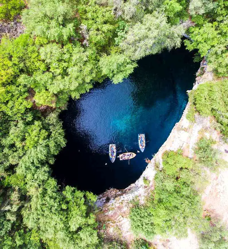 Aerial view of Melissani Cave's opening with trees and shrubs around the opening