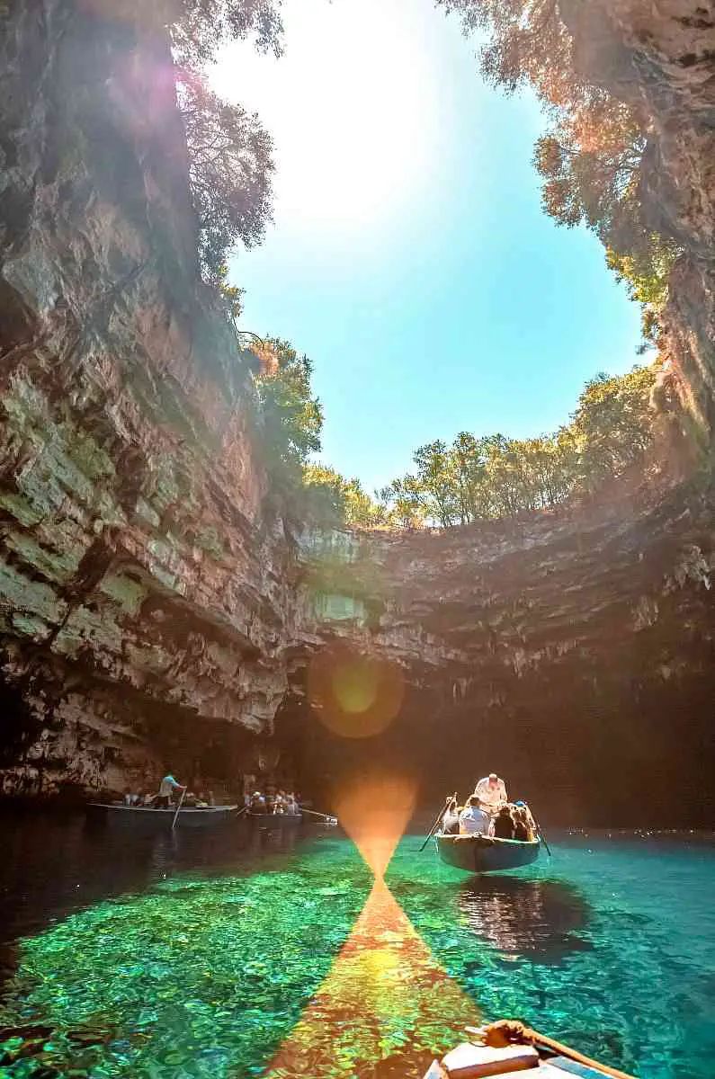 Melissani Lake with light shining through the opening in the cave roof with boats in the background
