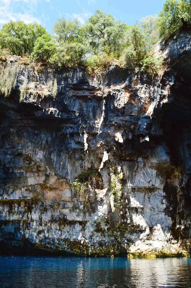 Sides of Melissani Cave with shrubs and trees on the top by the opening